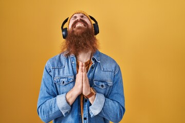 Caucasian man with long beard listening to music using headphones begging and praying with hands...