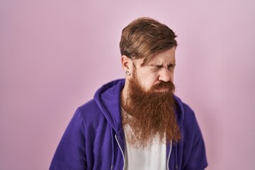 Caucasian man with long beard standing over pink background with hand on stomach because nausea, painful disease feeling unwell. ache concept.