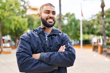 Young hispanic man standing with arms crossed gesture at park