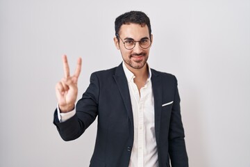 Handsome business hispanic man standing over white background showing and pointing up with fingers number two while smiling confident and happy.