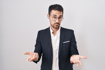 Handsome business hispanic man standing over white background clueless and confused with open arms, no idea concept. - obrazy, fototapety, plakaty