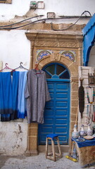 Clothing and souvenirs in front of a blue, wooden door in the Medina in Essaouira, Morocco