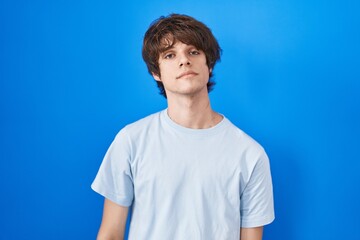 Hispanic young man standing over blue background relaxed with serious expression on face. simple and natural looking at the camera.