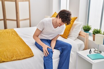 Young hispanic man suffering for knee pain at bedroom