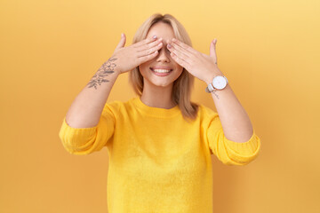 Young caucasian woman wearing yellow sweater covering eyes with hands smiling cheerful and funny. blind concept.