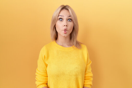 Young caucasian woman wearing yellow sweater making fish face with lips, crazy and comical gesture. funny expression.