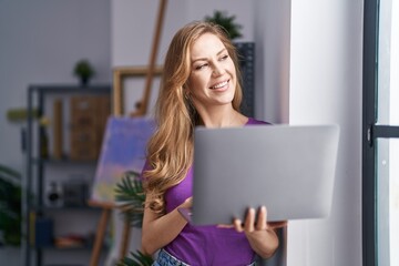 Young blonde woman artist smiling confident using laptop at art studio
