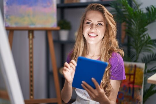Young blonde woman artist smiling confident using touchpad at art studio