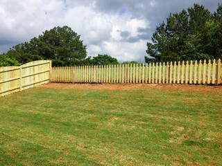 Wooden fence surrounds sloped backyard of new construction home.