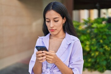 Young beautiful hispanic woman using smartphone with serious expression at street