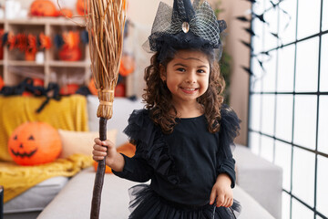 Adorable hispanic girl having halloween party holding broom at home