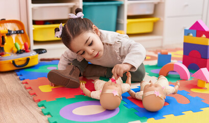 Adorable hispanic girl sitting on floor playing with baby doll at kindergarten