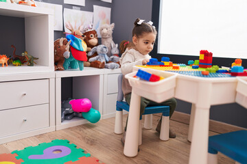 Adorable hispanic girl playing with construction blocks sitting on table at kindergarten