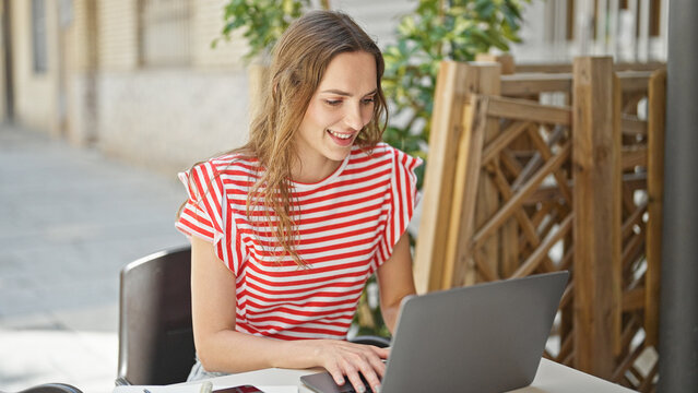 Young blonde woman using laptop sitting on table at coffee shop terrace