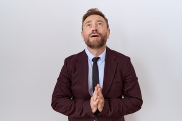 Middle age business man with beard wearing suit and tie begging and praying with hands together with hope expression on face very emotional and worried. begging.