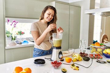 Young beautiful hispanic woman preparing vegetable smoothie with blender at the kitchen