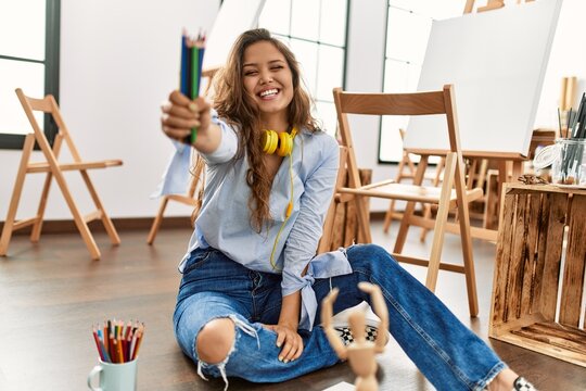Young beautiful hispanic woman artist smiling confident holding pencils at art studio