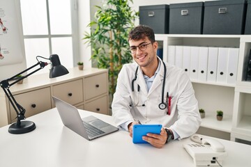 Young hispanic man doctor using laptop and touchpad working at clinic