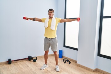 Fototapeta na wymiar Young hispanic man smiling confident using dumbbells training at sport center