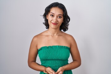 Young hispanic woman standing over isolated background with hands together and crossed fingers smiling relaxed and cheerful. success and optimistic