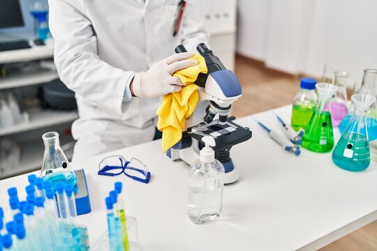 Young hispanic man scientist cleaning microscope at laboratory
