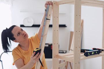 Woman assembling new wooden shelf and furniture in the apartment.