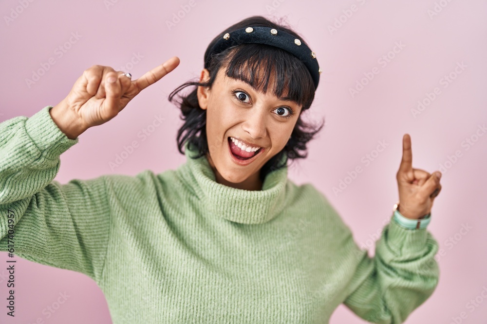 Sticker young beautiful woman standing over pink background smiling amazed and surprised and pointing up wit