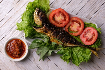 grilled fish and fresh vegetables. lettuce, sliced tomatoes, basil leaves, green onions. Indonesian food. ikan bakar.
