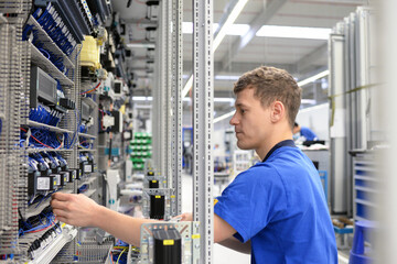 young operator assembles machine in a modern high tech factory - production of switch cabinets for...