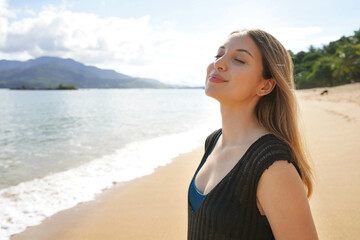 Portrait of young lady breathing with closed eyes enjoys sunbathe on the beach. Relax and sunbathing in Ilhabela Island, Brazil.