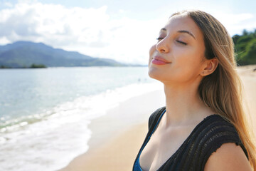 Young woman breathing with closed eyes enjoys sunbathe on the beach. Relax and sunbathing holidays...