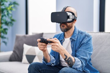 Young bald man playing video game using virtual reality glasses at home