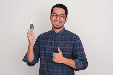 Adult Asian man smiling proud and give thumb up while holding a car key - obrazy, fototapety, plakaty