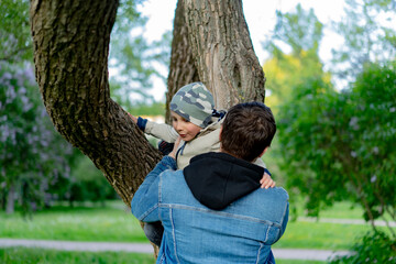  A father helping his cute little son go down a tree in park . Image with selective focus.