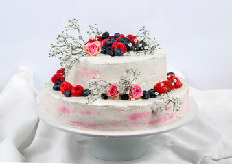 eine zweistöckige Hochzeitstorte mit Beeren und Blumen verzierte festliche Sahnetorte auf hellem Hintergrund