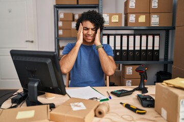 Hispanic man with curly hair working at small business ecommerce with hand on head, headache because stress. suffering migraine.