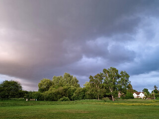 View of dark storm clouds rolling in over green trees and grass fields