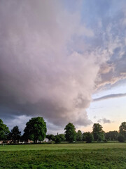 View of dark storm clouds rolling in over green trees and grass fields