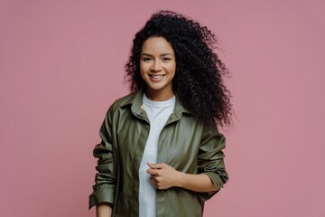 Smiling Afro-American woman in leather shirt, enjoying day with friends, curly hair. Isolated on pink.