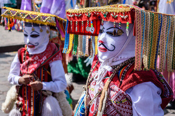 Cusco, a cultural fiesta, people dressed in traditional colourful costumes with masks and hats, brightly coloured streamers.