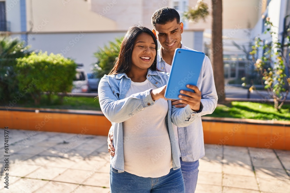 Poster Young latin couple expecting baby using touchpad at park