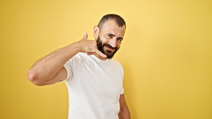 Young hispanic man smiling confident doing telephone gesture with hand over isolated yellow background