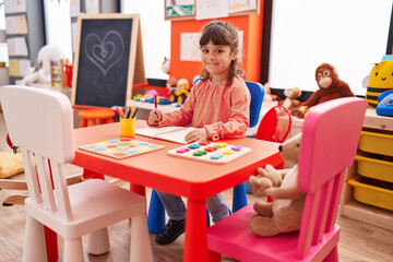 Obraz na płótnie Canvas Adorable hispanic girl student sitting on table drawing on notebook at kindergarten