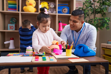 Hispanic man with boy and girl playing with construction blocks sitting on table at kindergarten