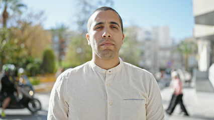 Young hispanic man sitting on a bench with serious expression at street