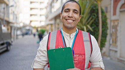 Young hispanic man volunteer smiling holding clipboard at street - Powered by Adobe