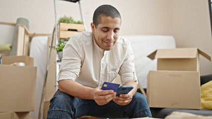 Young hispanic man smiling confident using smartphone doing online shopping at new home