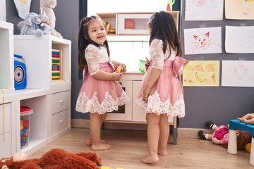 Adorable twin girls playing with play kitchen standing at kindergarten