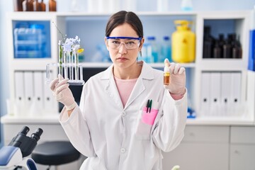 Young brunette woman working at scientist laboratory skeptic and nervous, frowning upset because of...