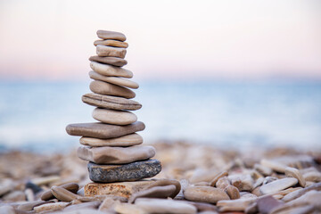 Fototapeta na wymiar The pebble tower balances harmony stones on the Aegean sea beach at sunset. Relaxing peaceful spa tranquility concept with copy space for text 